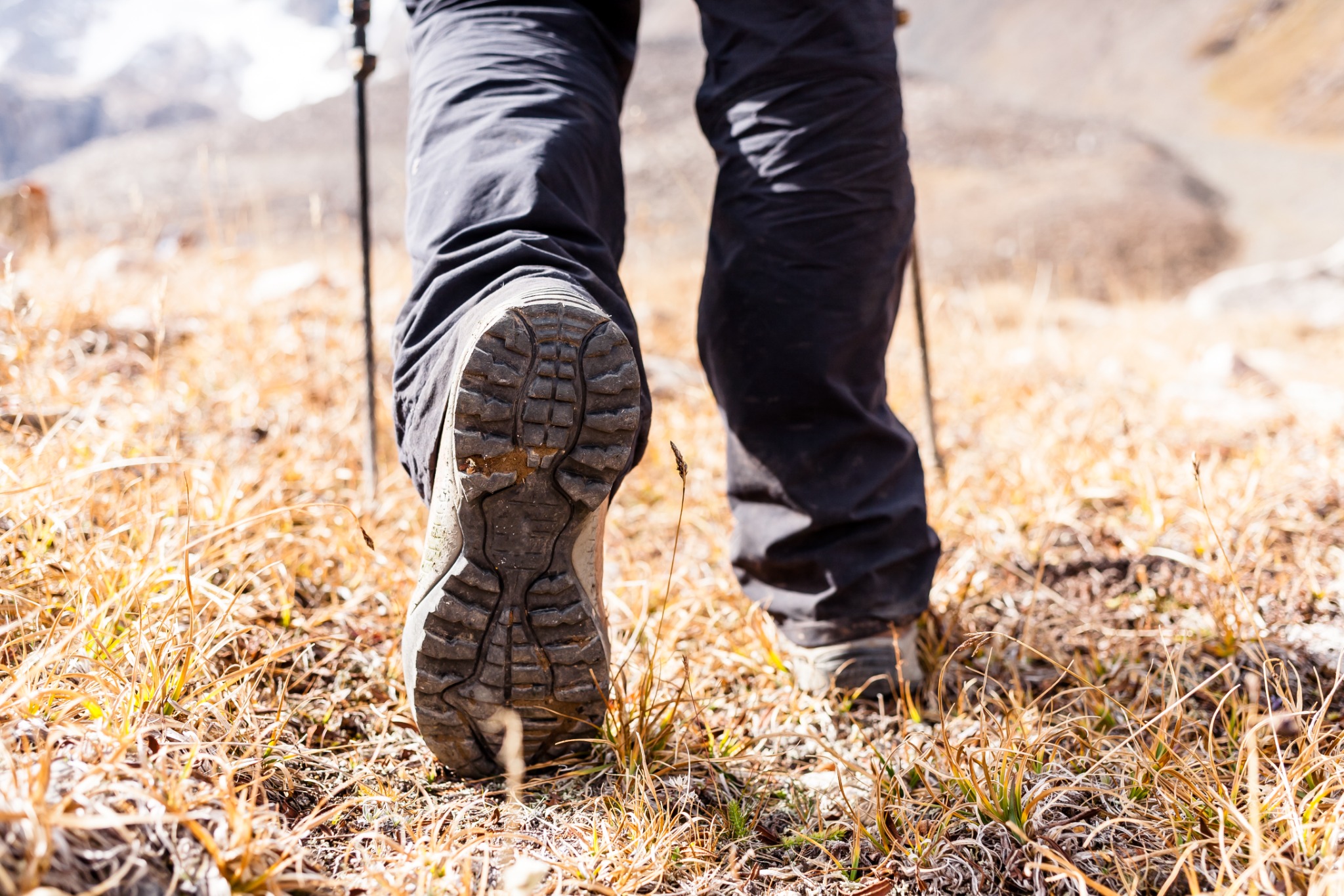 Senderista avanzando por un sendero de montaña con botas y bastones